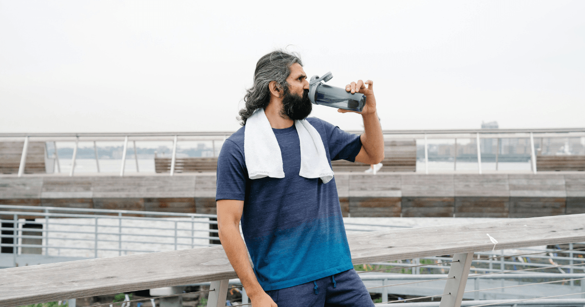 A man with a beard drinks water from a bottle, showcasing a moment of refreshment and relaxation.