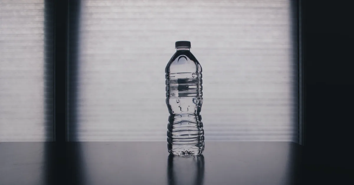A bottle of water placed on a table, illuminated by natural light streaming through a nearby window.