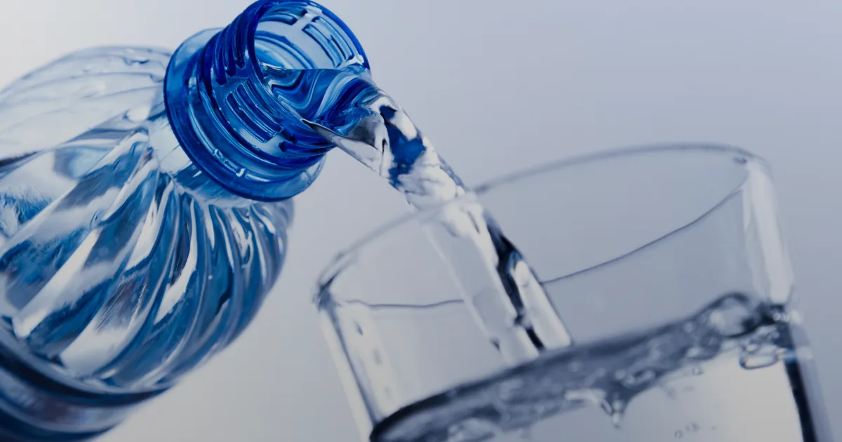 A bottle of water is being poured into a clear glass, creating a splash as it fills.