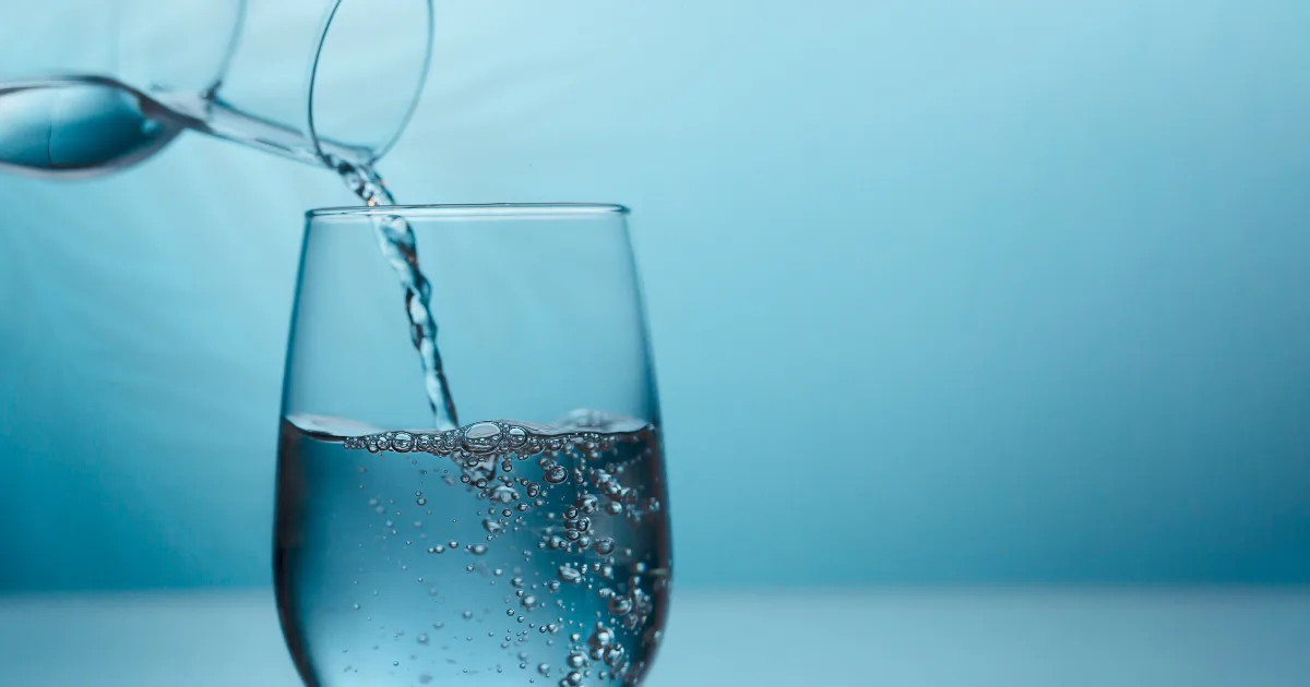 A clear glass being filled with water from a pouring jug, capturing the moment of liquid flowing into the glass.