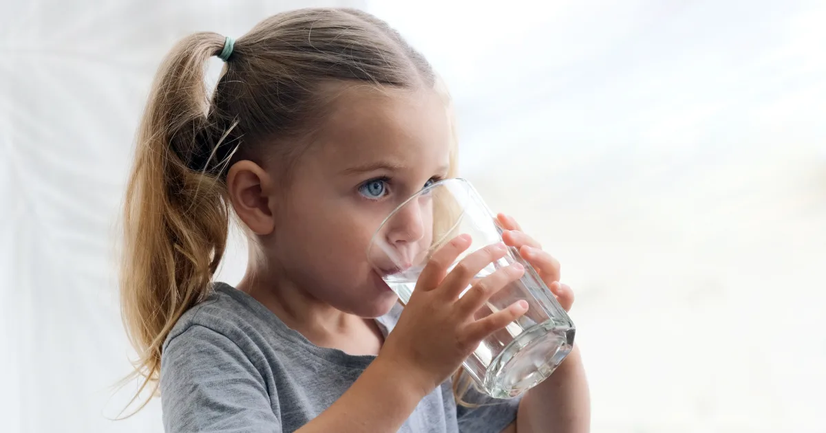 A young girl happily drinking water from a clear glass, showcasing a moment of refreshment and joy.