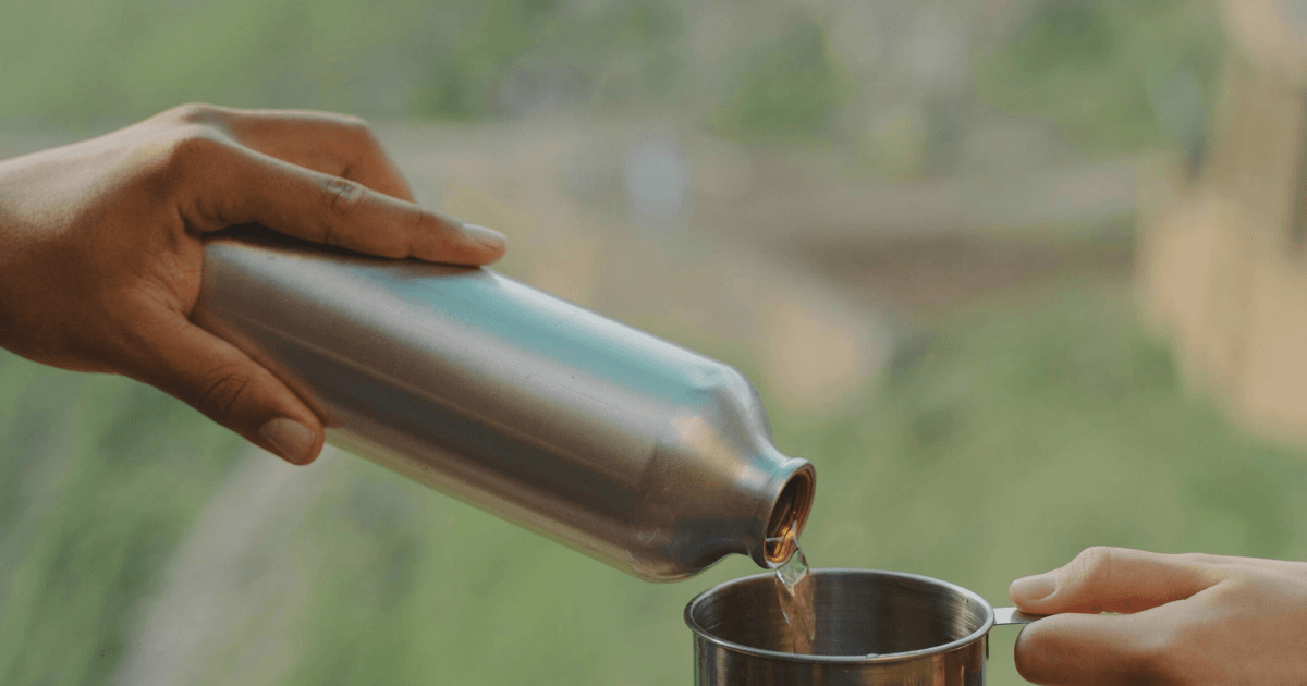 A person pouring tea from a teapot into a stainless steel bottle, showcasing a blend of tradition and modernity.