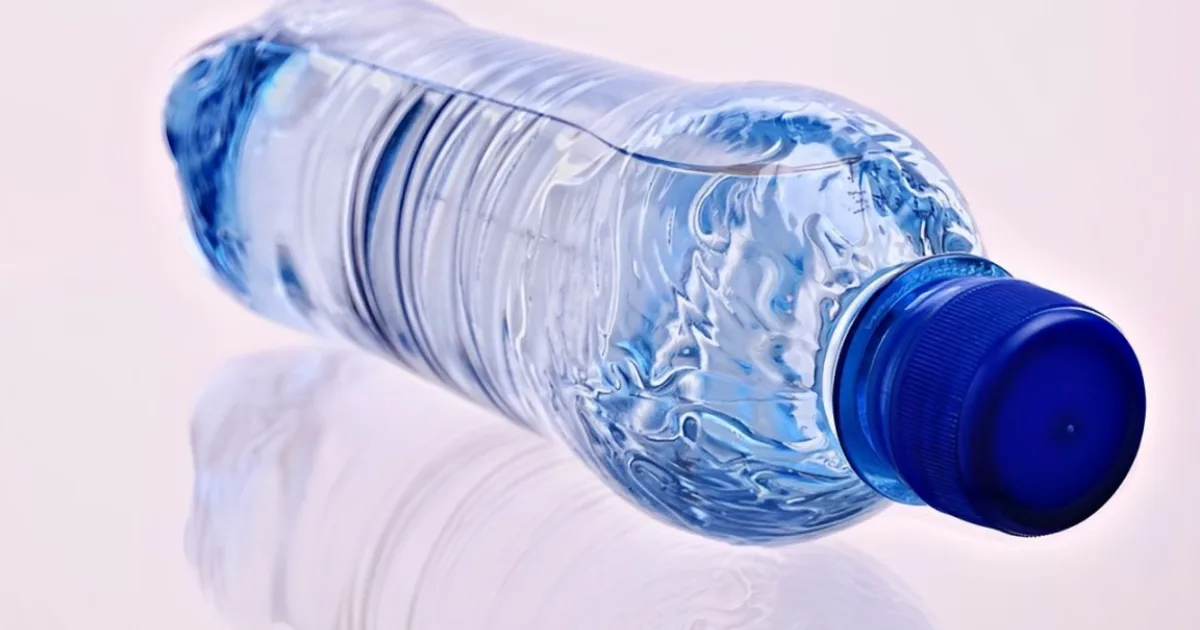 A plastic bottle of water placed on a wooden table, reflecting natural light in a serene setting.