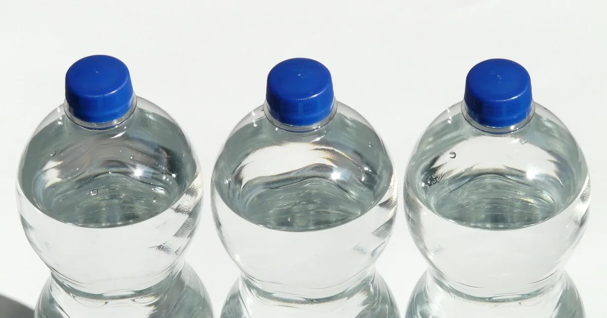 Three bottles of water with blue caps arranged neatly on a surface, showcasing their clear contents and vibrant caps.