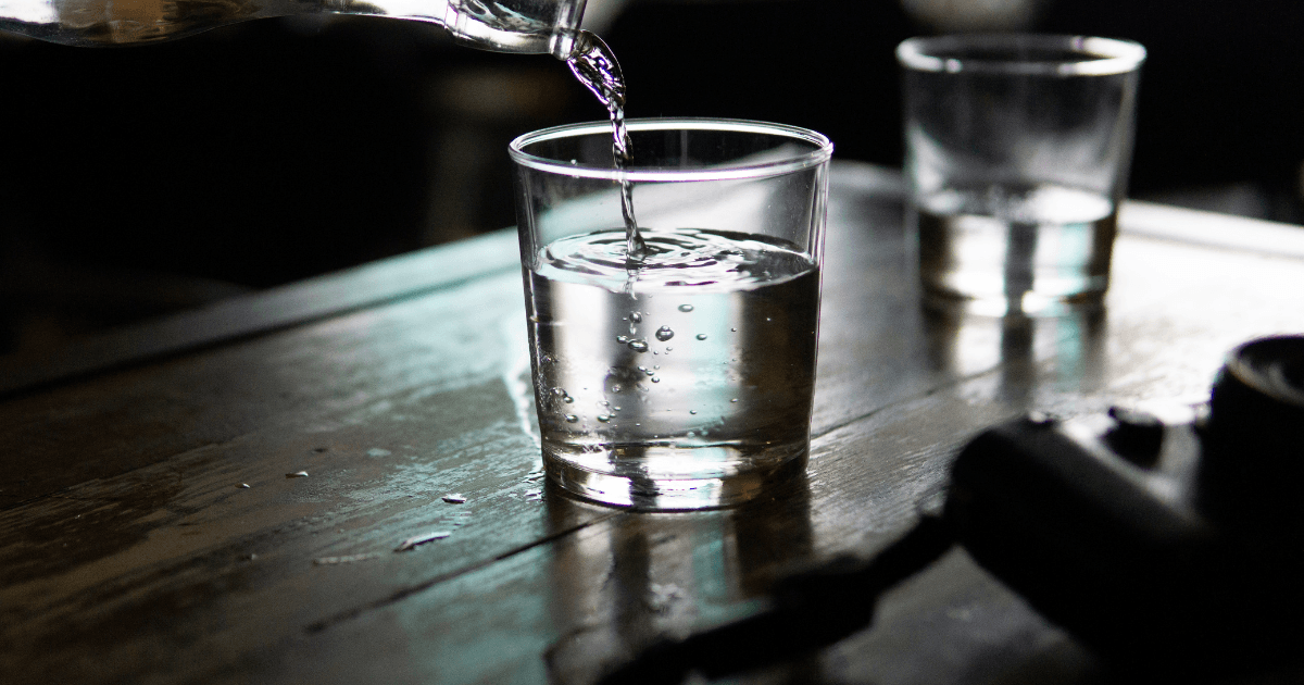 A person carefully pours water from a pitcher into a clear glass, capturing the moment of refreshment.