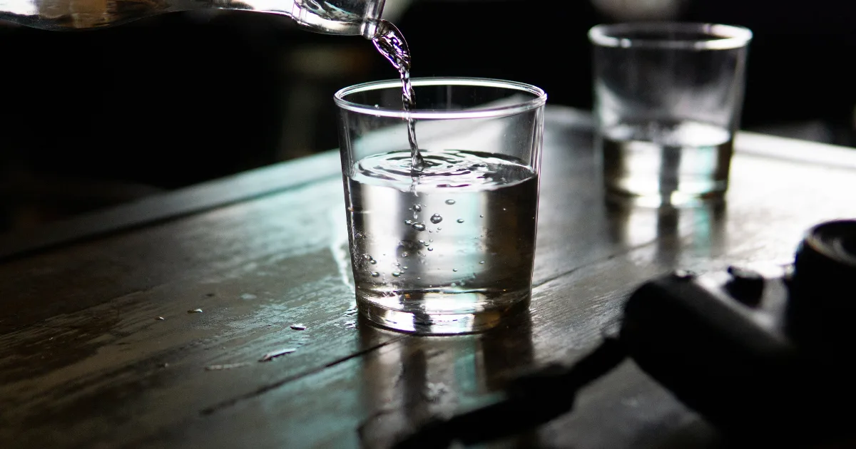 A person carefully pours water from a pitcher into a clear glass, capturing the moment of refreshment.