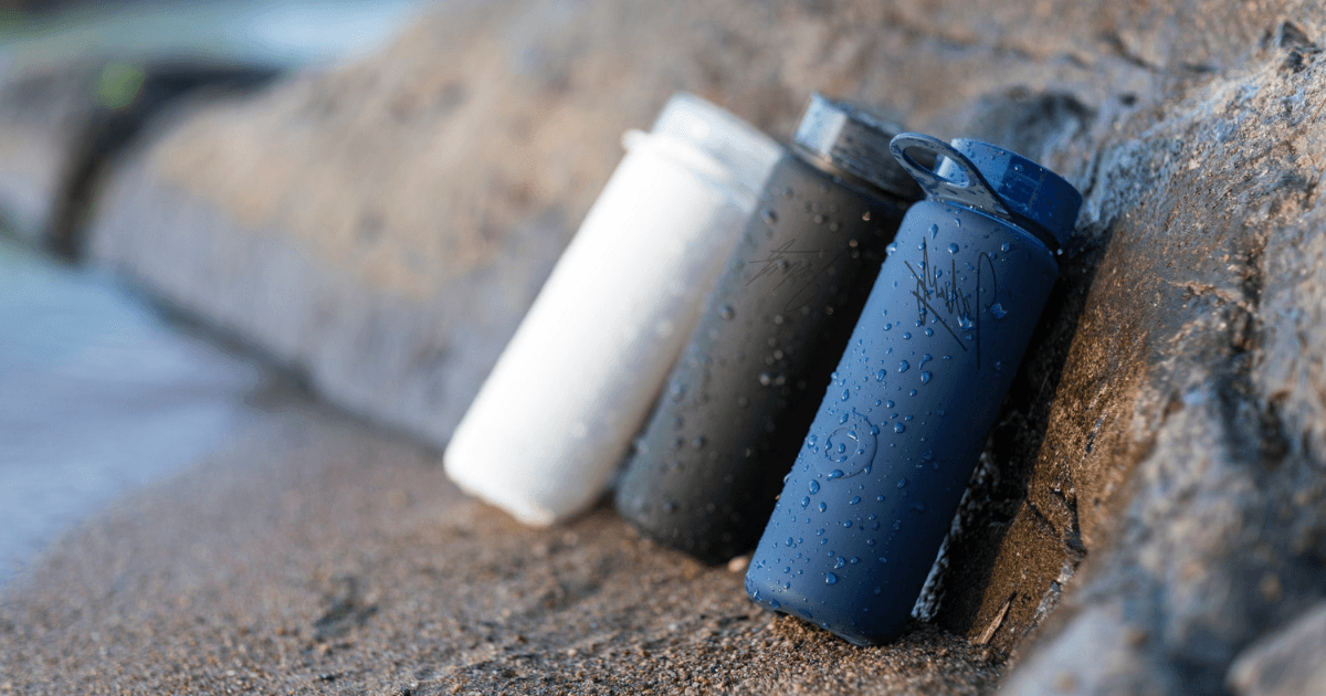 Three water bottles placed on a rock, showcasing their vibrant colors against a natural outdoor backdrop.