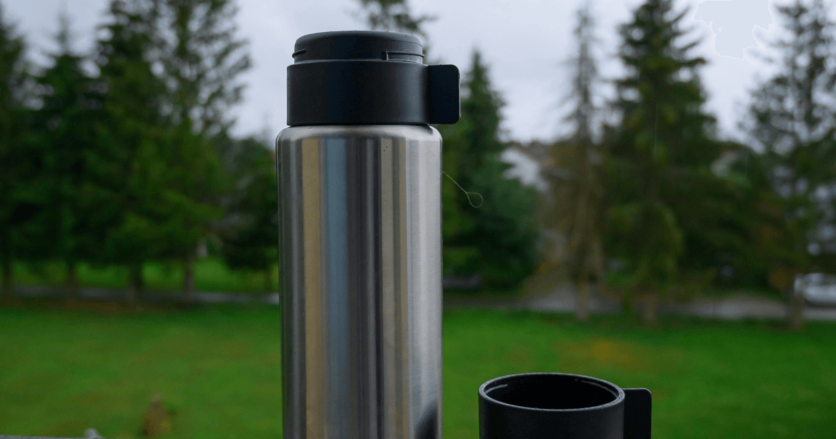 A stainless steel water bottle beside a sleek black cup on a neutral background, showcasing modern drinkware.