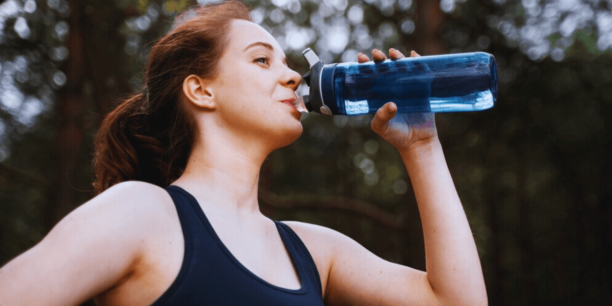 A woman refreshing herself by drinking water from a clear water bottle, promoting hydration and wellness.