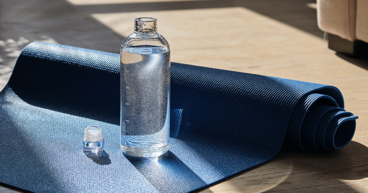 A bottle of water placed beside a rolled yoga mat on a clean surface, promoting hydration and wellness.