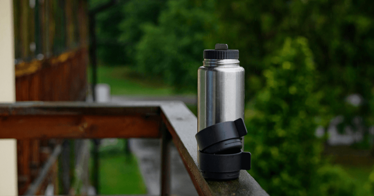 A stainless steel water bottle rests on a wooden railing, showcasing a blend of modern design and natural materials.