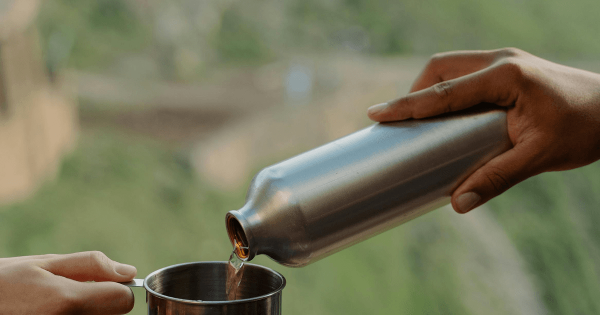 A person pouring tea from a teapot into a stainless steel bottle, showcasing a blend of tradition and modernity.
