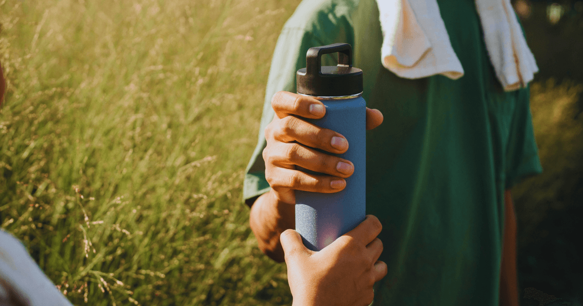 A man holds a water bottle while standing in front of another man wearing a green shirt.