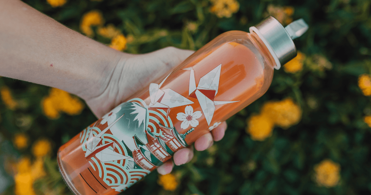 A person is holding an orange water bottle featuring a unique design, showcasing hydration and style.