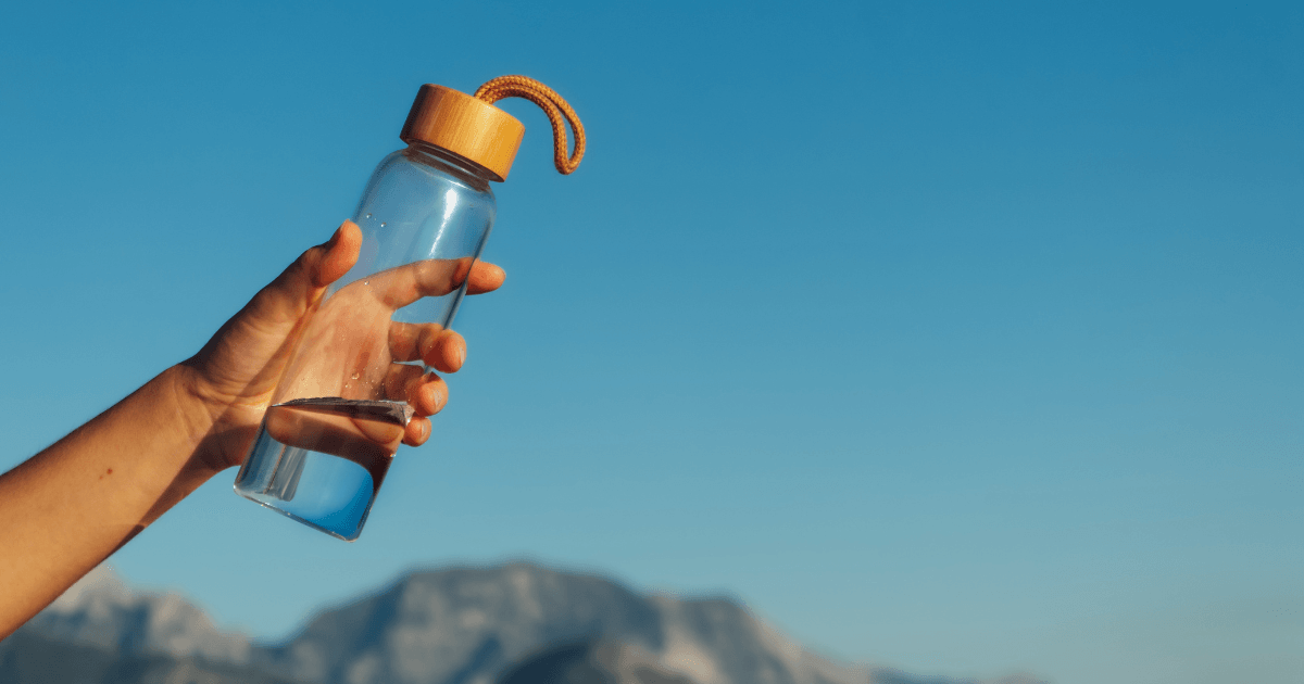 A person holds a water bottle, with majestic mountains rising in the background, showcasing a connection to nature.
