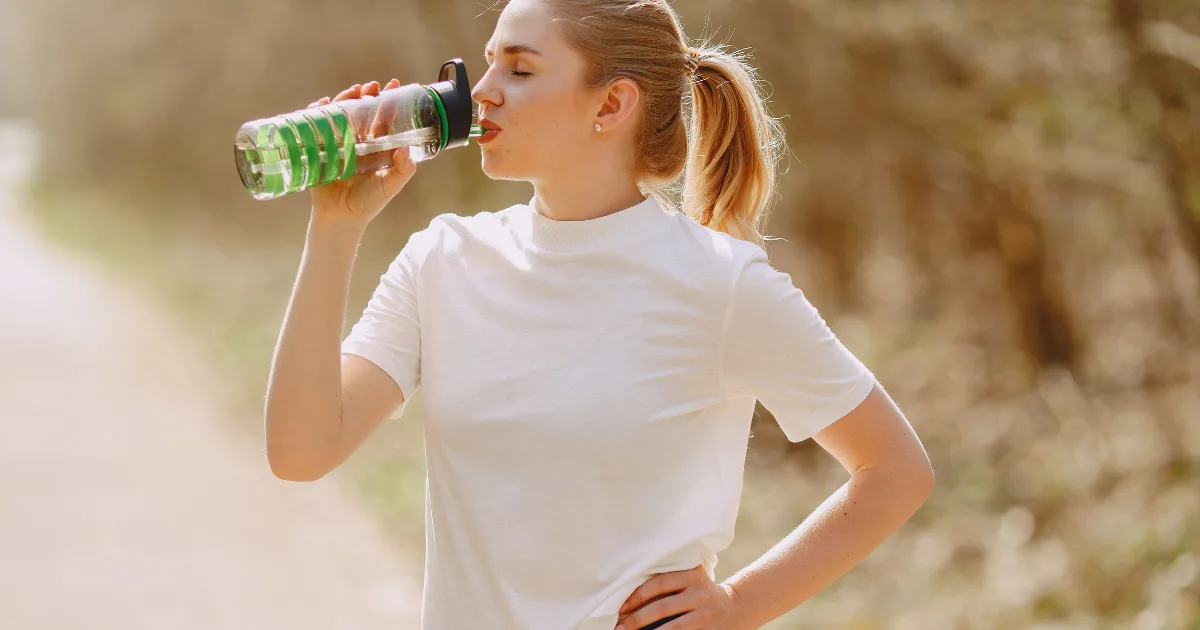 A woman refreshing herself by drinking water from a clear bottle, promoting hydration and wellness.