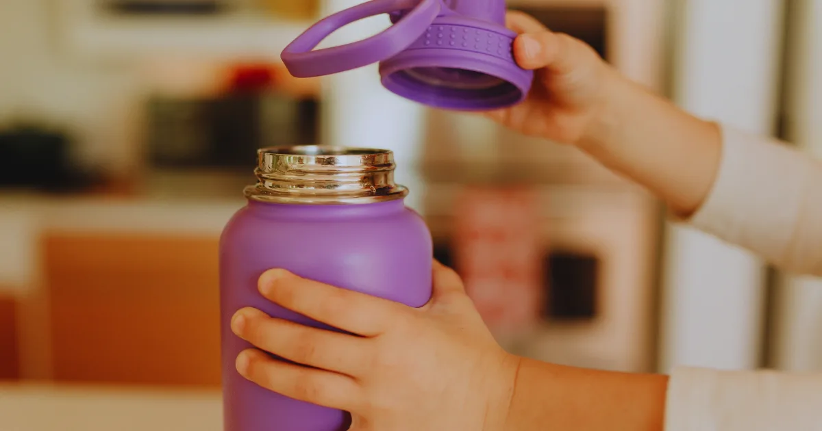 A child is holding a purple water bottle with a secure lid, showcasing a playful and active lifestyle.