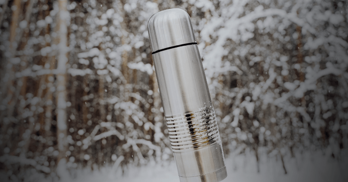 A silver flask rests elegantly on a blanket of pristine snow, reflecting the surrounding winter landscape.