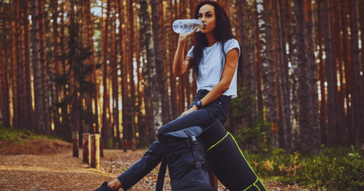 A girl drinking from fiji water bottle with a beautiful jungle background.