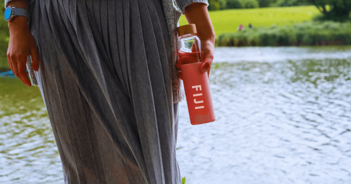 A girl holding fiji water bottle in her hand with beautiful river background.