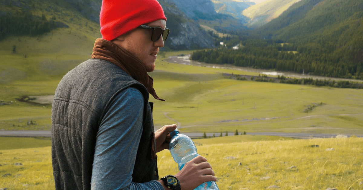 A man holding fiji water bottle with a mountains background.