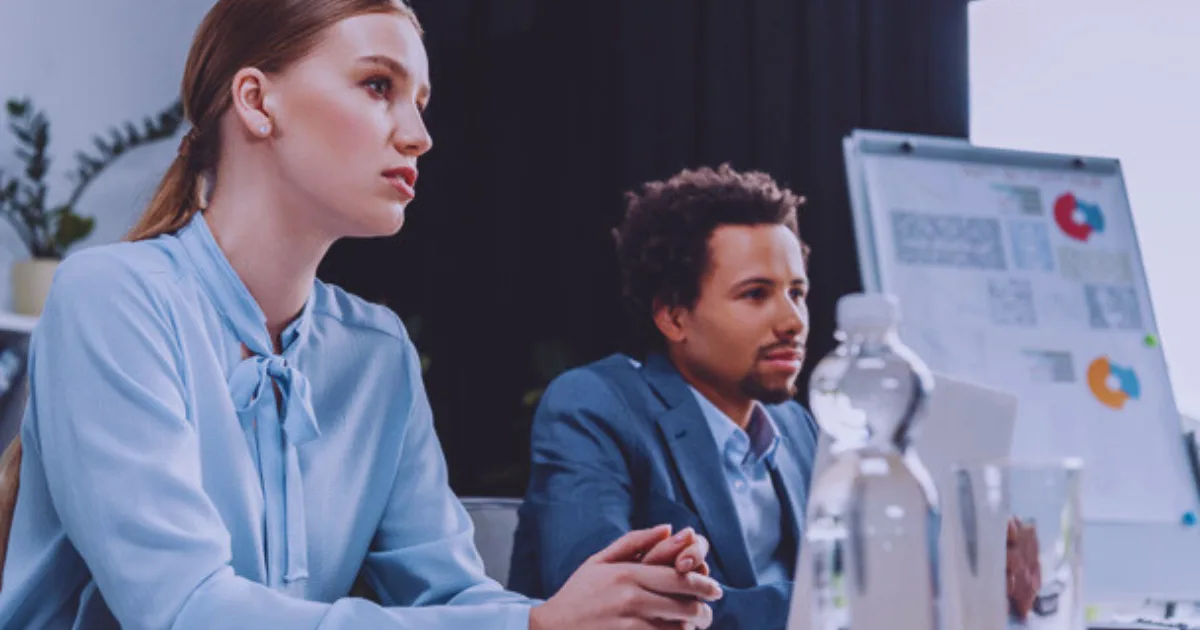 A woman and a man are seated at a table, engaged with a water bottle in front of them.
