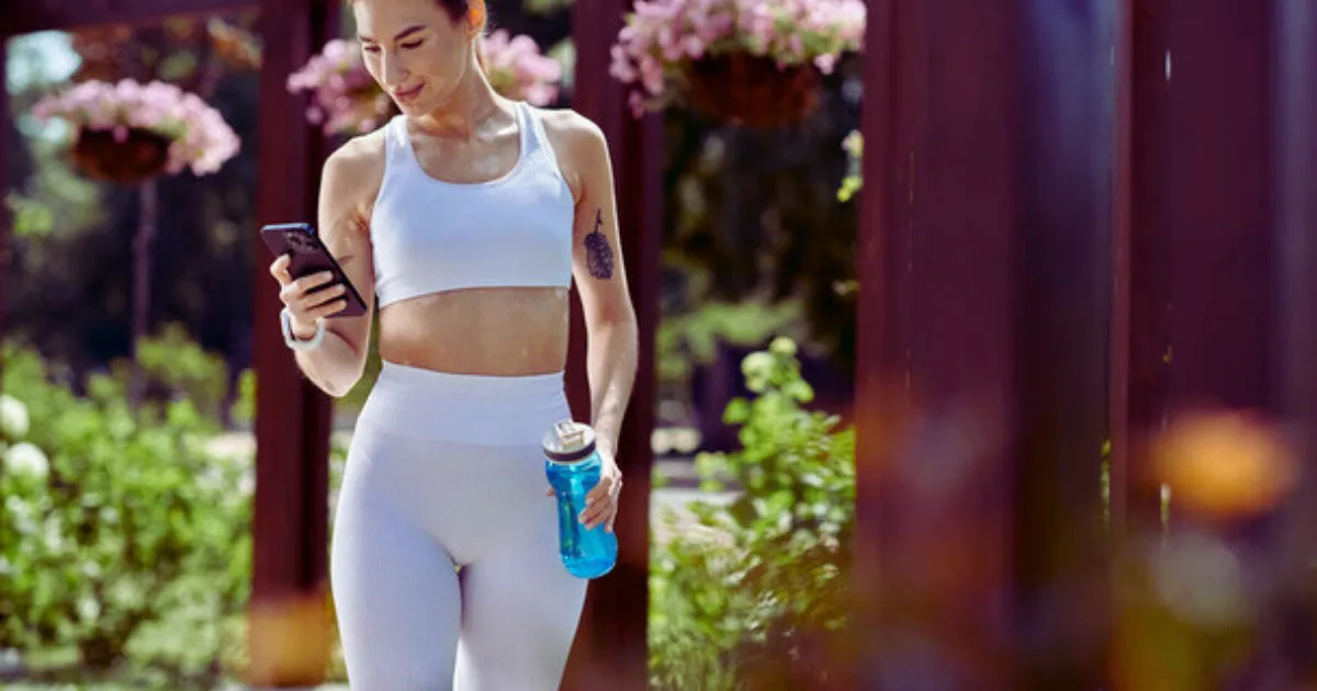 A woman in white sports attire is holding a cell phone, appearing focused and ready for her workout.