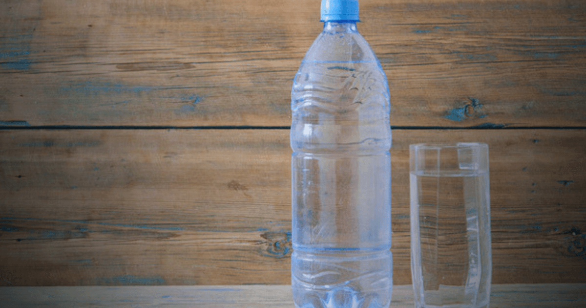 A bottle of water beside a glass on a rustic wooden table, showcasing a simple and refreshing setting.