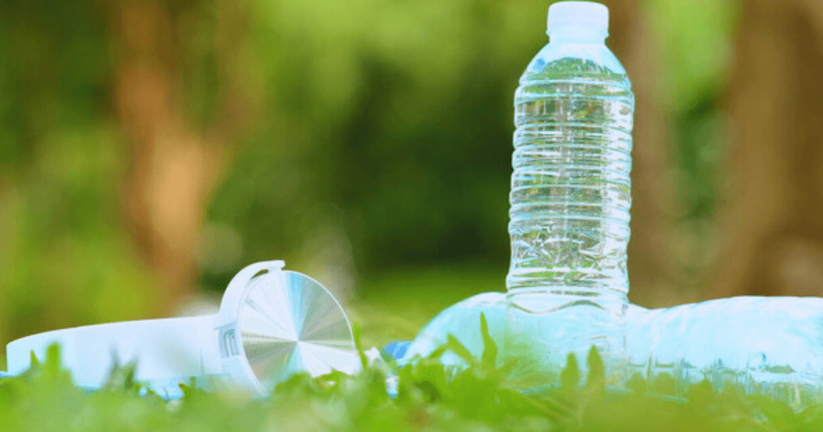 A plastic bottle and a plastic cup resting on green grass, highlighting environmental concerns about plastic waste.