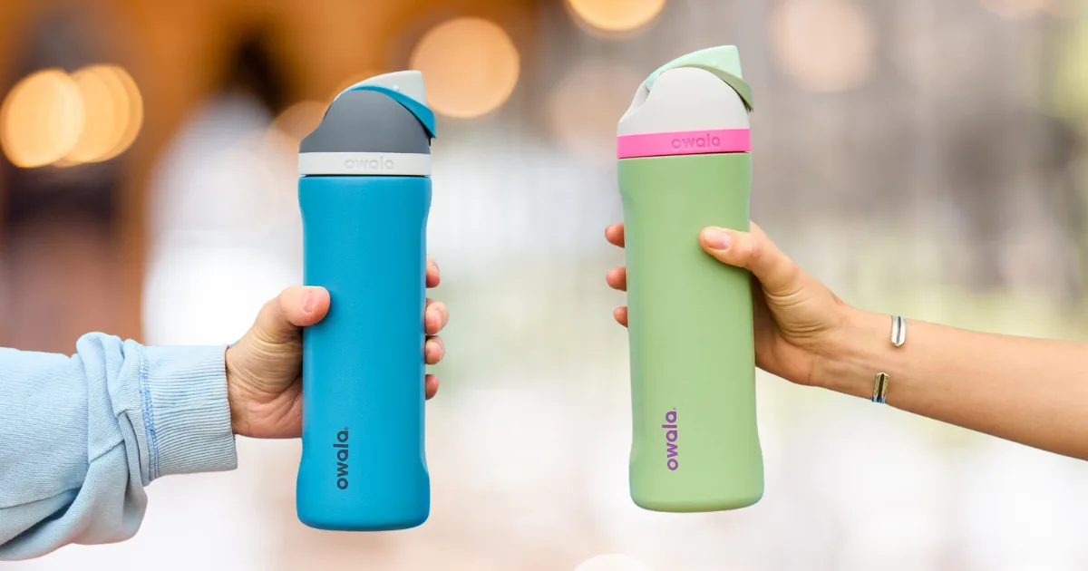Two hands hold Owala water bottles, the ultimate hydration solution, against a blurred backdrop. In one hand is a blue and gray bottle, while the other cradles a vibrant green and pink one. Both feature convenient flip-top lids for easy sipping on the go.