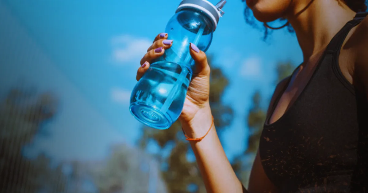 A woman drinks from an Owala water bottle, enjoying hydration on a sunny day outdoors.